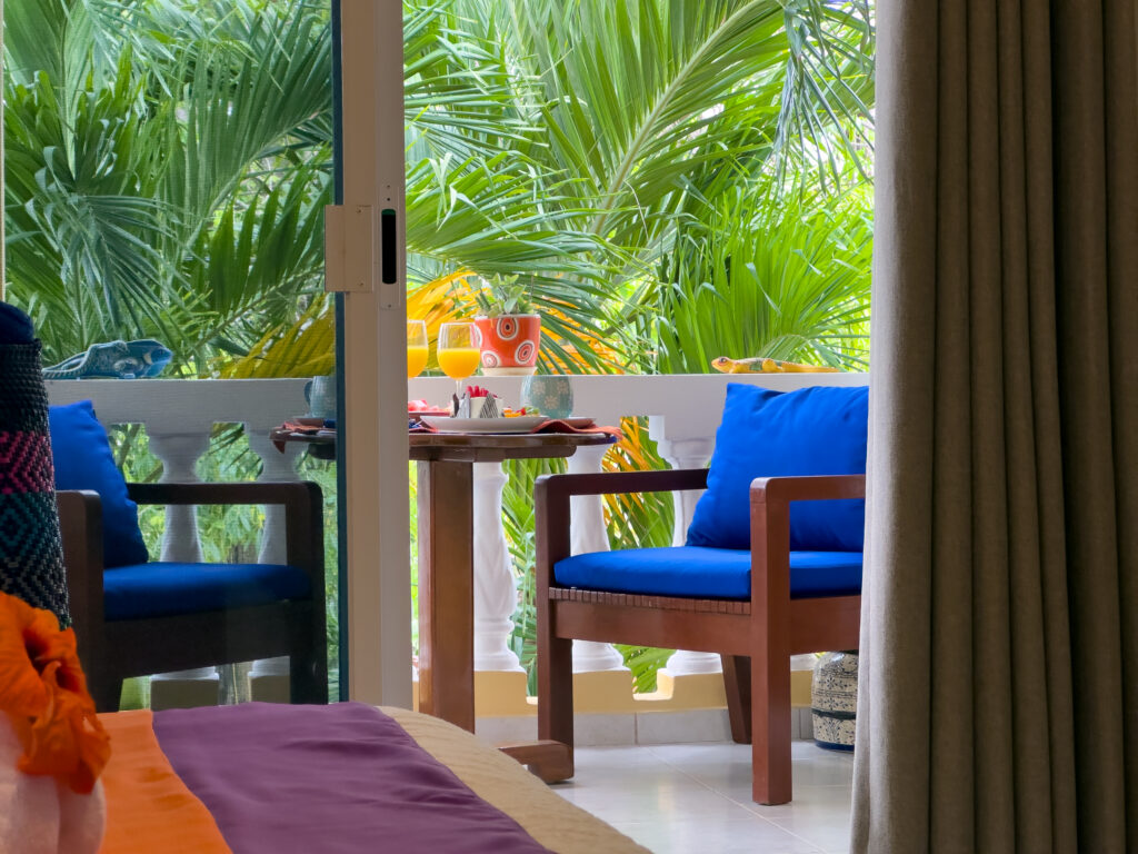 Two blue-cushioned wooden chairs and a small table framed by dense palm fronds.