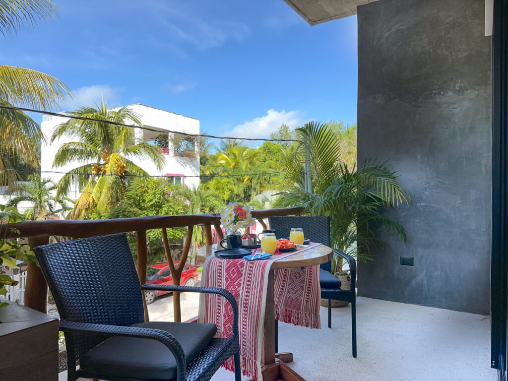 Small outdoor dining table set with dishes beneath blue skies and palm fronds.