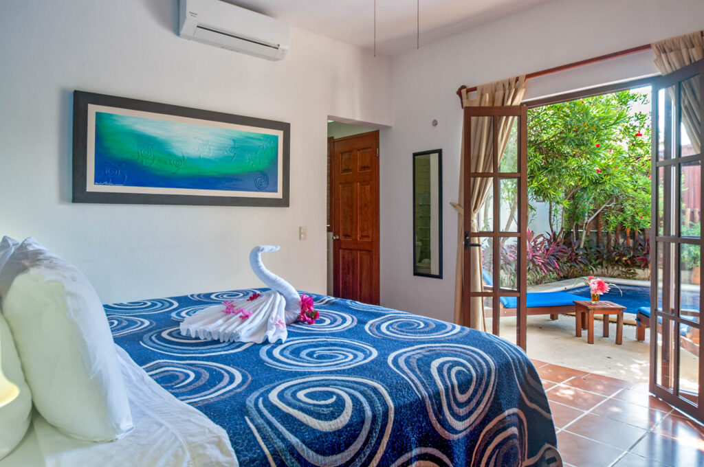 Bed with a blue spiral-patterned cover and towel swan beside open doors to the pool patio.