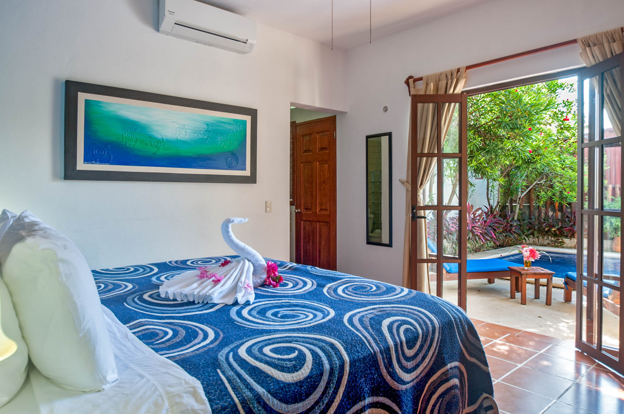 Bed with a blue spiral-patterned cover and towel swan beside open doors to the pool patio.