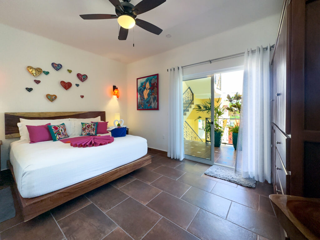 Bed with pink accents beside glass doors opening onto a balcony with potted plants.