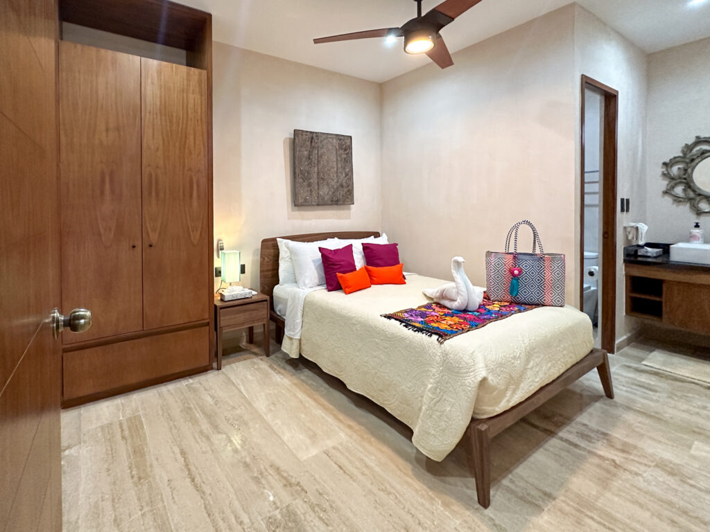 Wooden bed with colorful pillows and towel decoration beside a vanity with an ornate round mirror.