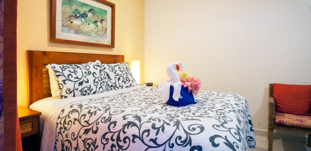Patterned bedspread with folded towel decorations beneath framed artwork.