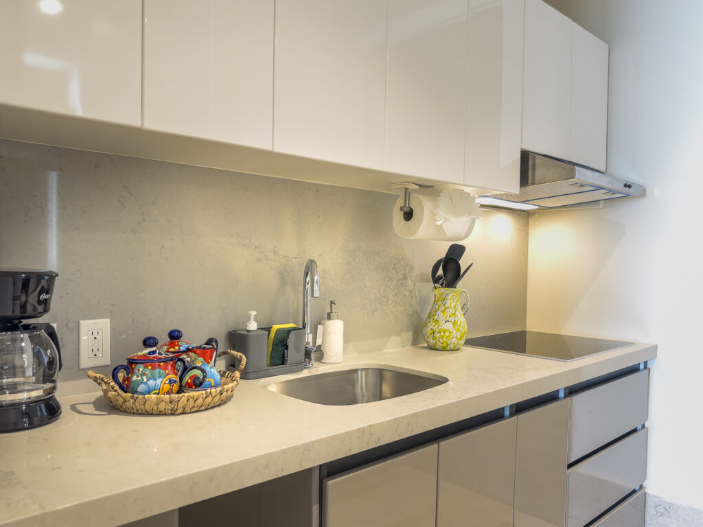 Kitchen counter with a coffee maker, sink, utensils, and cooktop beneath white cabinets.