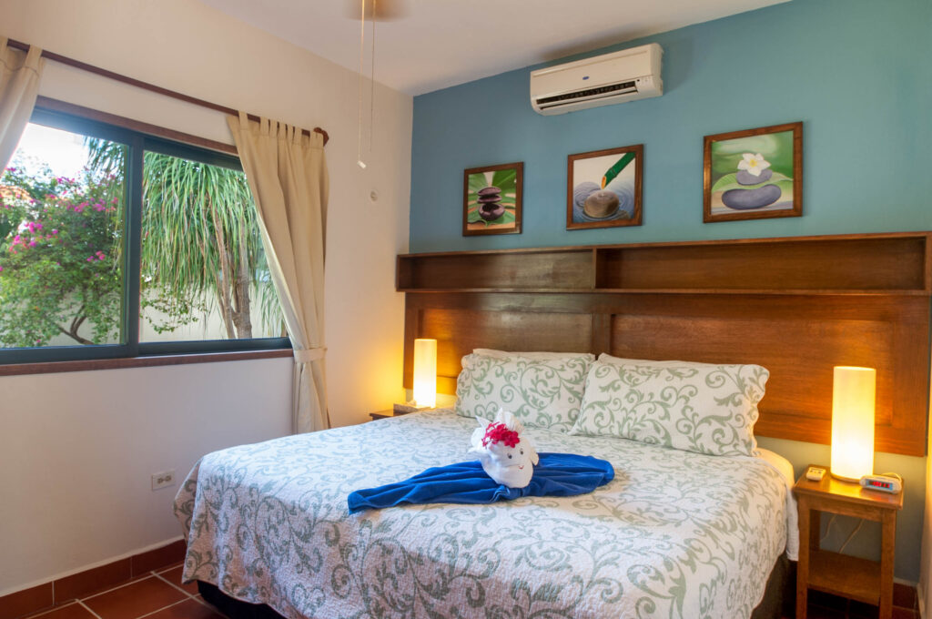 Bed with pale patterned bedding beneath three small framed pictures beside a garden window.