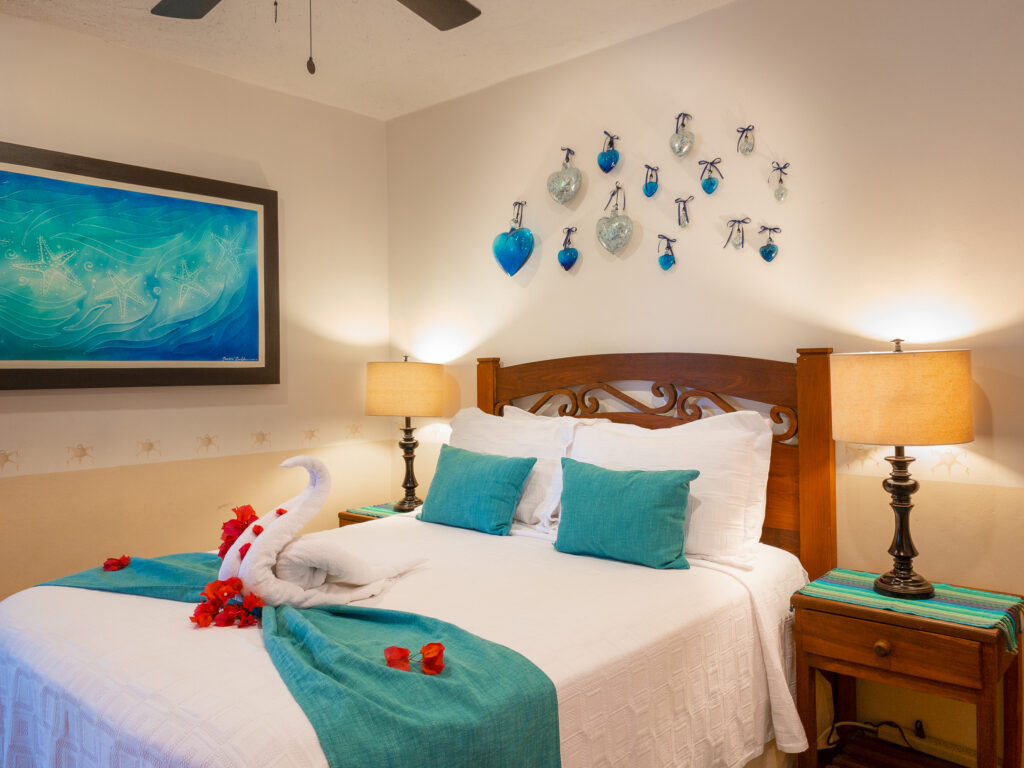 Bed with turquoise accents and folded towel decoration beside blue artwork and matching lamps.