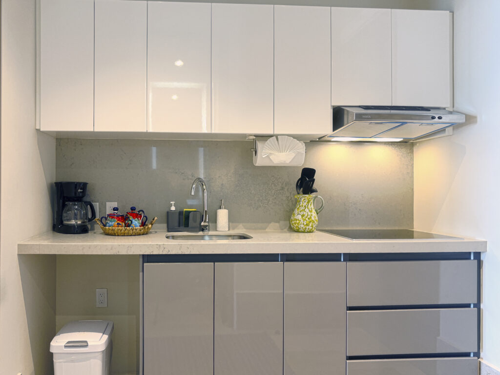 White kitchen cabinets above a sink, coffee maker, and cooktop with an overhead hood.