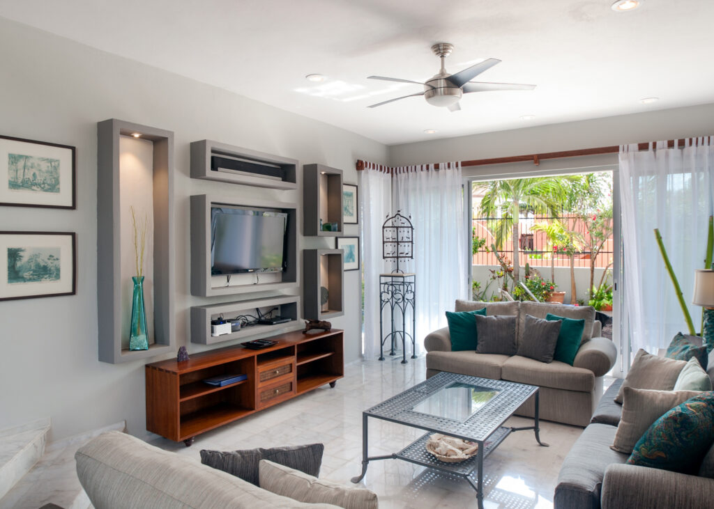 Living room seating faces a television near glass doors opening to greenery.