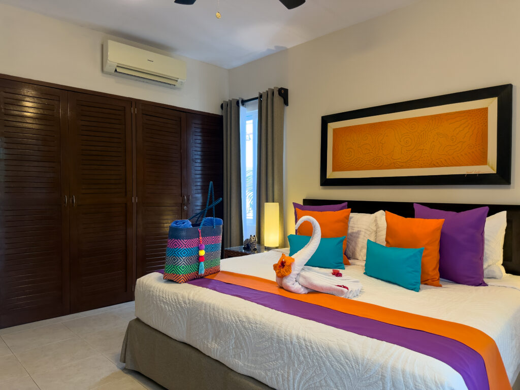 Bed with orange and purple accents beside dark wooden closet doors.