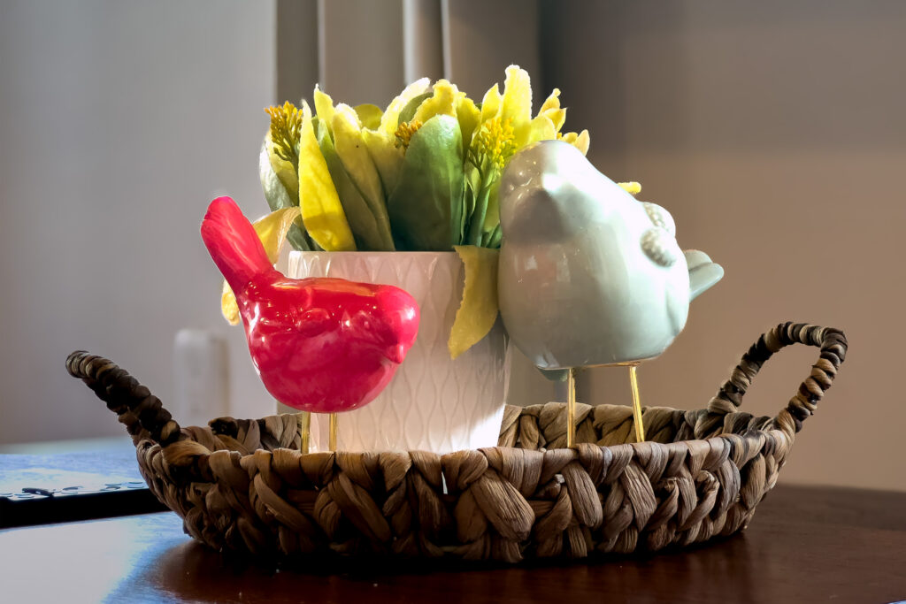 Colorful ceramic birds and a small vase of flowers arranged on a woven tray.