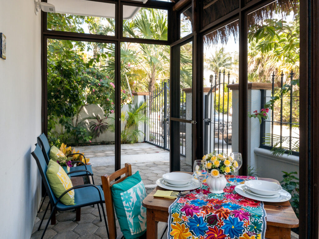 Dining table and blue chairs inside a screened patio overlooking plants and a garden gate.