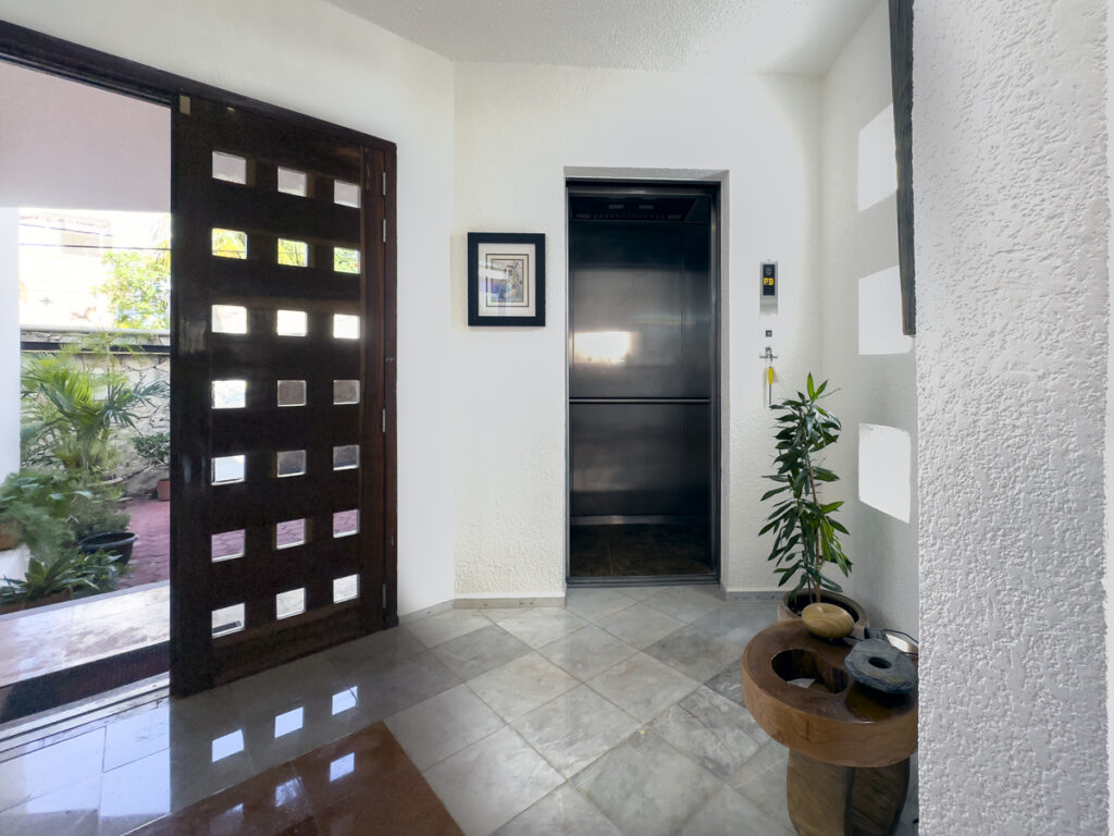 Open wooden front door beside a metal elevator door and a potted plant.