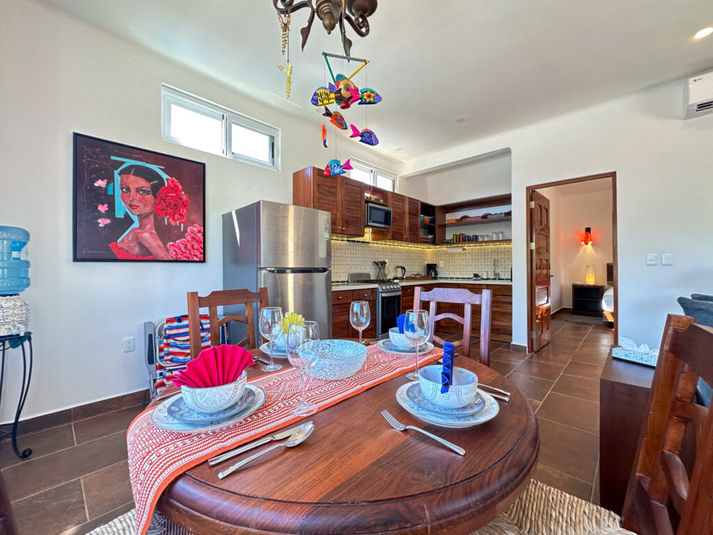Table set with dishes beside a stainless steel refrigerator and kitchen with wooden cabinets.