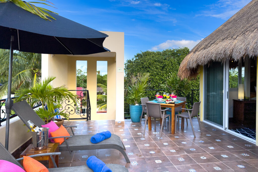 Tiled terrace with lounge chairs, a dark umbrella, potted palms, and an outdoor dining table.