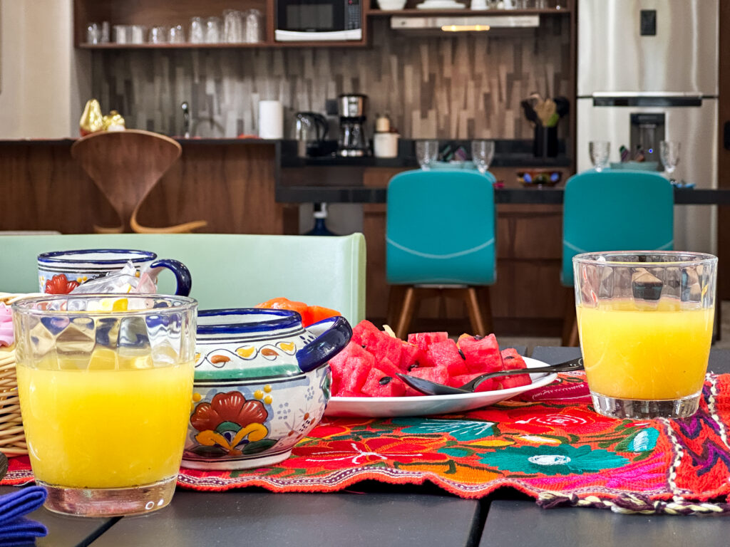 Glasses of orange juice and colorful ceramic dishes on a bright floral table runner.