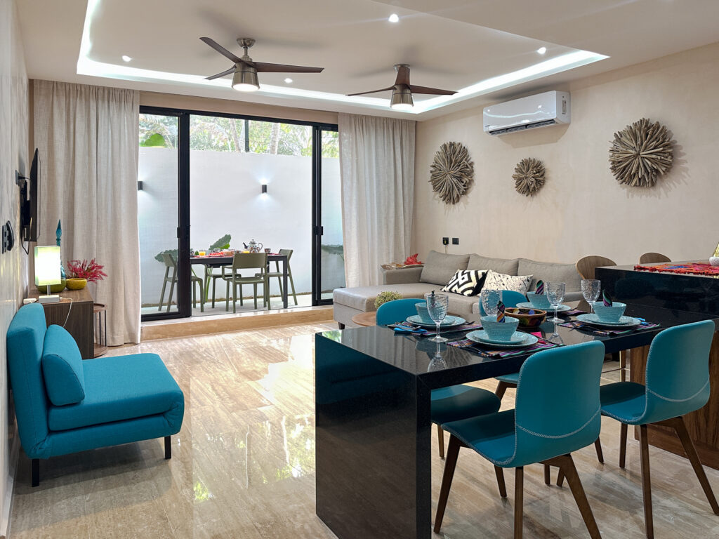 Gray sofa and dining table with turquoise chairs beside large glass doors opening to a patio.