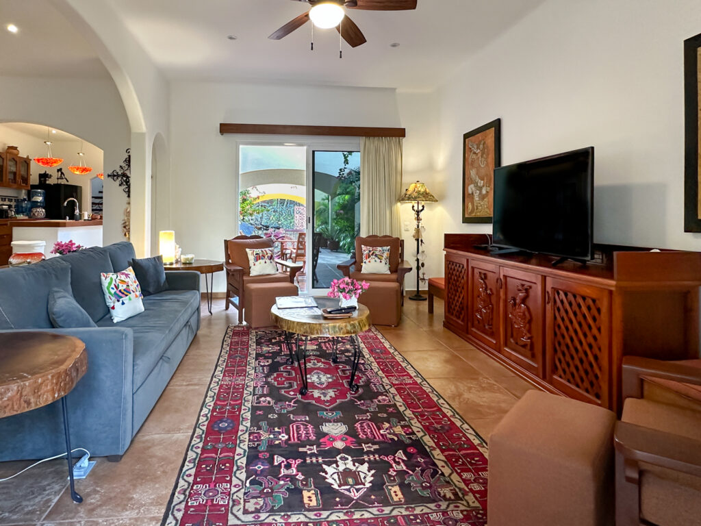 Sofa and armchairs around a patterned rug facing a television on a carved wooden console.