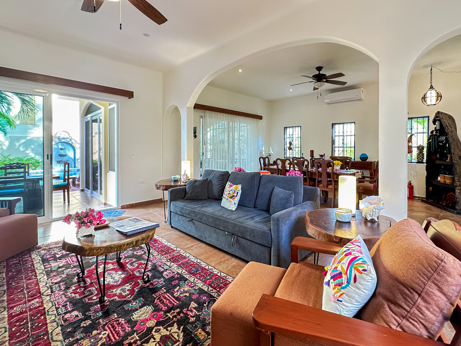 Blue sofa and wooden armchairs around a small table on a patterned rug beside arched dining-room openings.