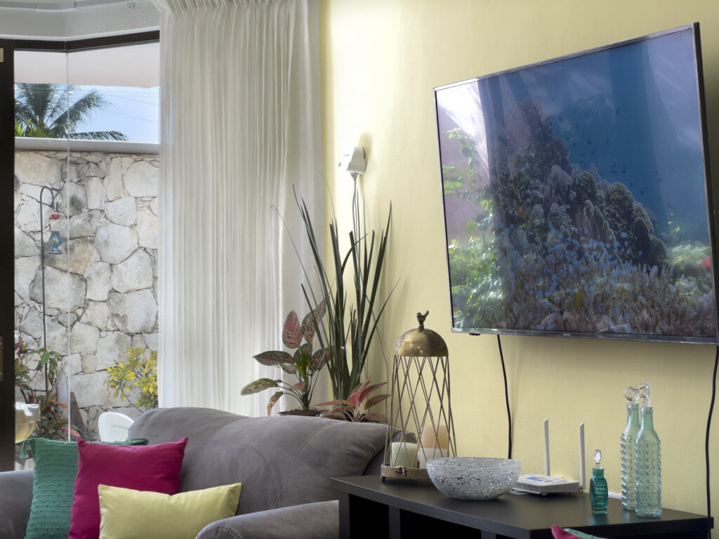 Wall-mounted television above a console with decorative glassware beside a gray sofa.