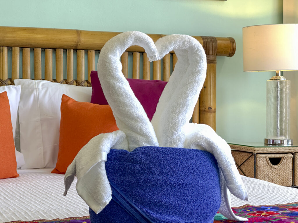 Two white towel swans form a heart above a blue towel on the bed.
