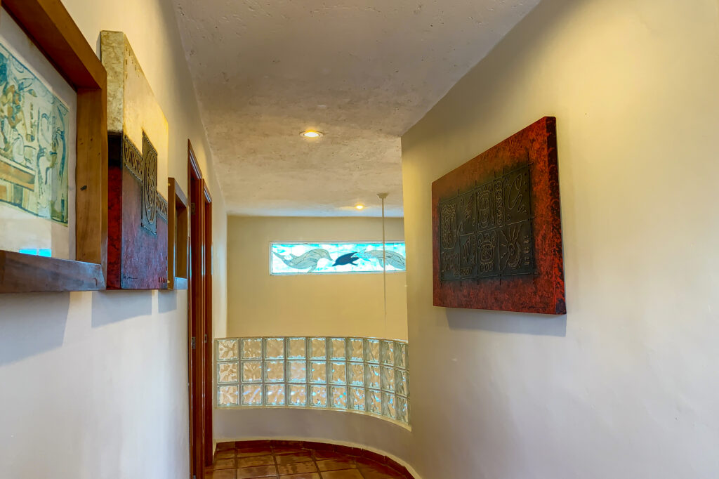 Narrow upstairs hallway with framed artwork and a glass-block wall at the stair landing.