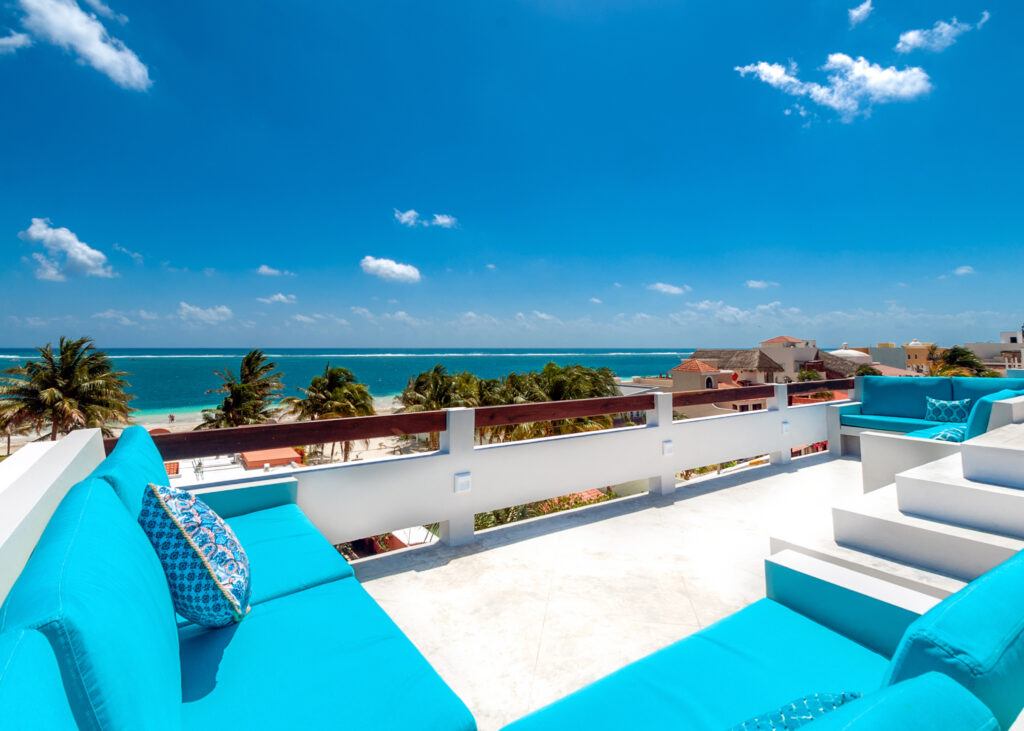 Turquoise built-in rooftop seating overlooks palm trees, rooftops, and the Caribbean Sea.