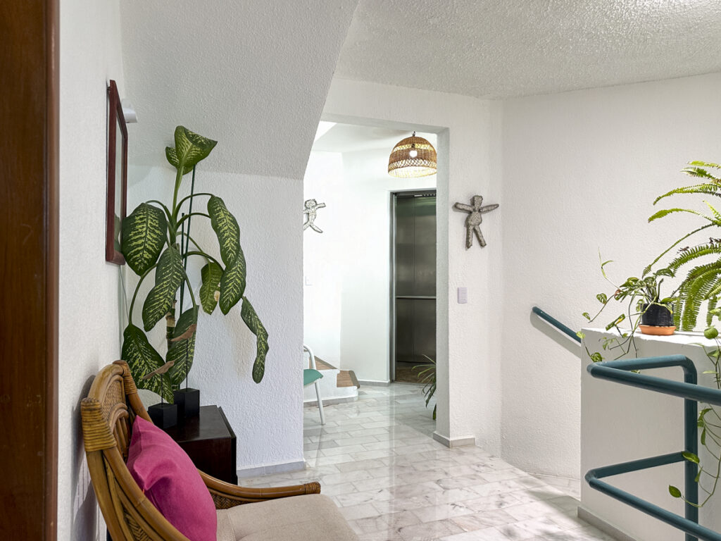 Upstairs landing with a wicker chair, potted plants, and teal stair railings.