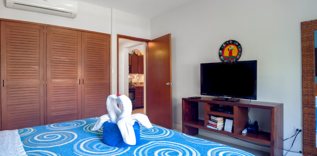 Bed with a towel swan facing a television cabinet and wooden closet doors.