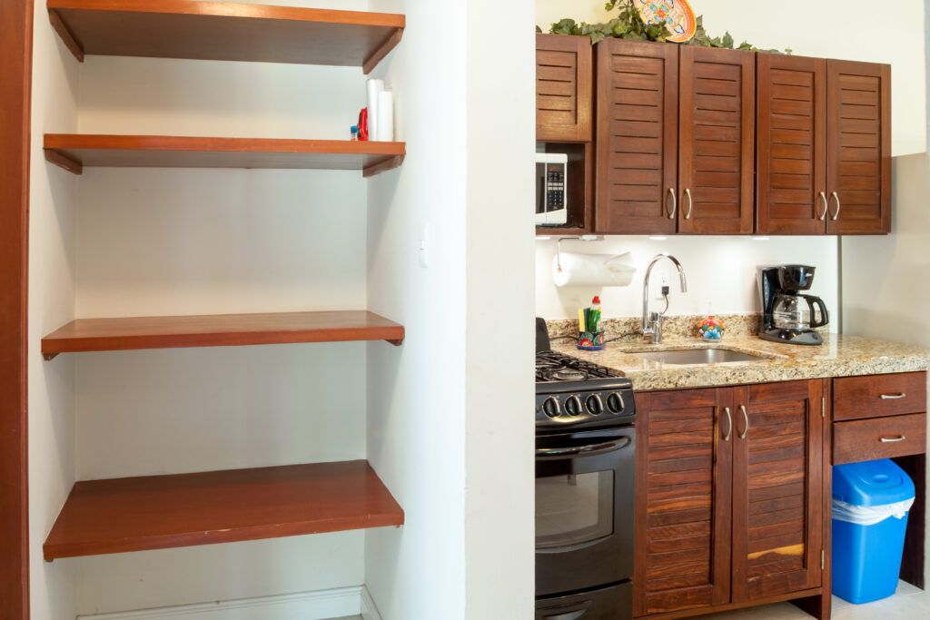 Open wooden shelves beside a kitchen counter, stove, and wooden cabinets.