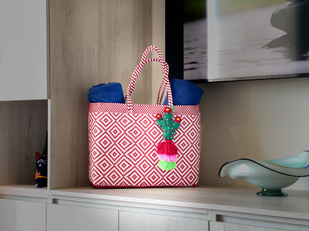Pink-and-white woven bag holding rolled blue towels beside the television cabinet.