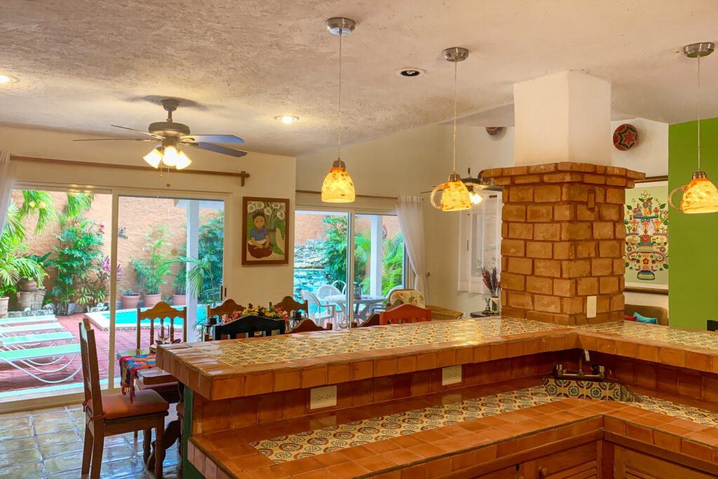 Tiled kitchen counter beside a brick column with dining space and glass garden doors beyond.
