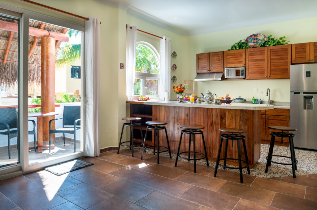Wooden kitchen cabinets and a long breakfast bar with stools beside balcony doors.