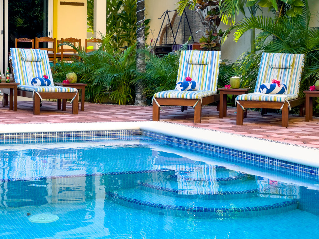 Curved pool steps in front of lounge chairs with striped cushions and rolled towels.