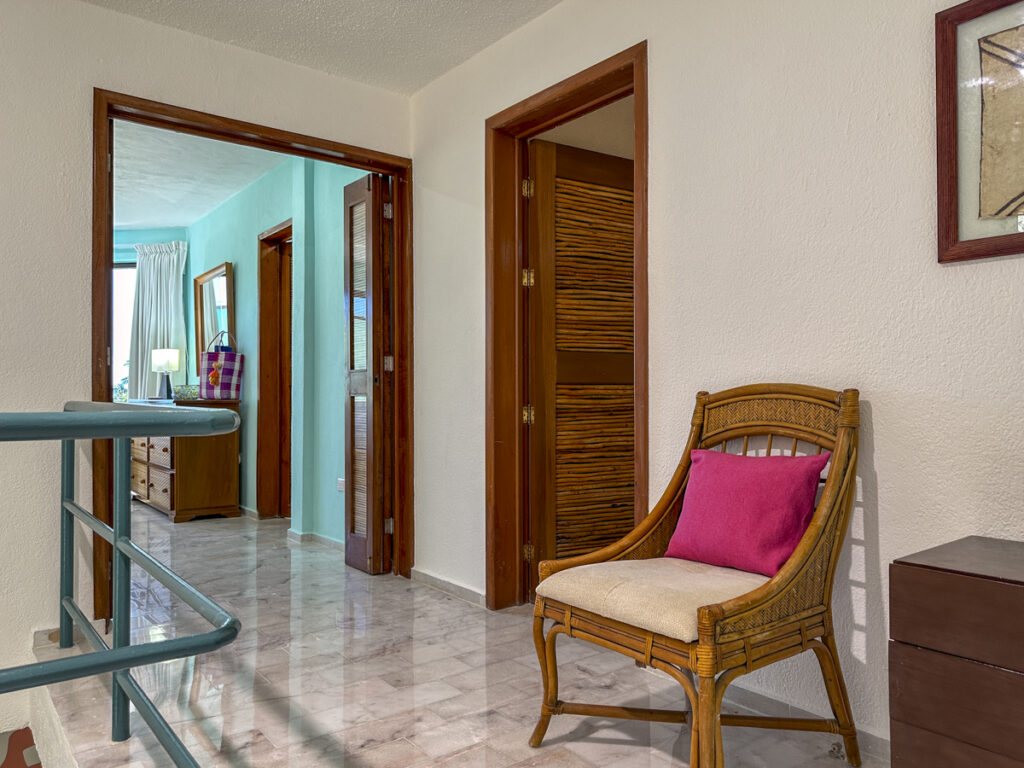 Wicker chair with a pink cushion beside open bedroom doorways along the upstairs landing.