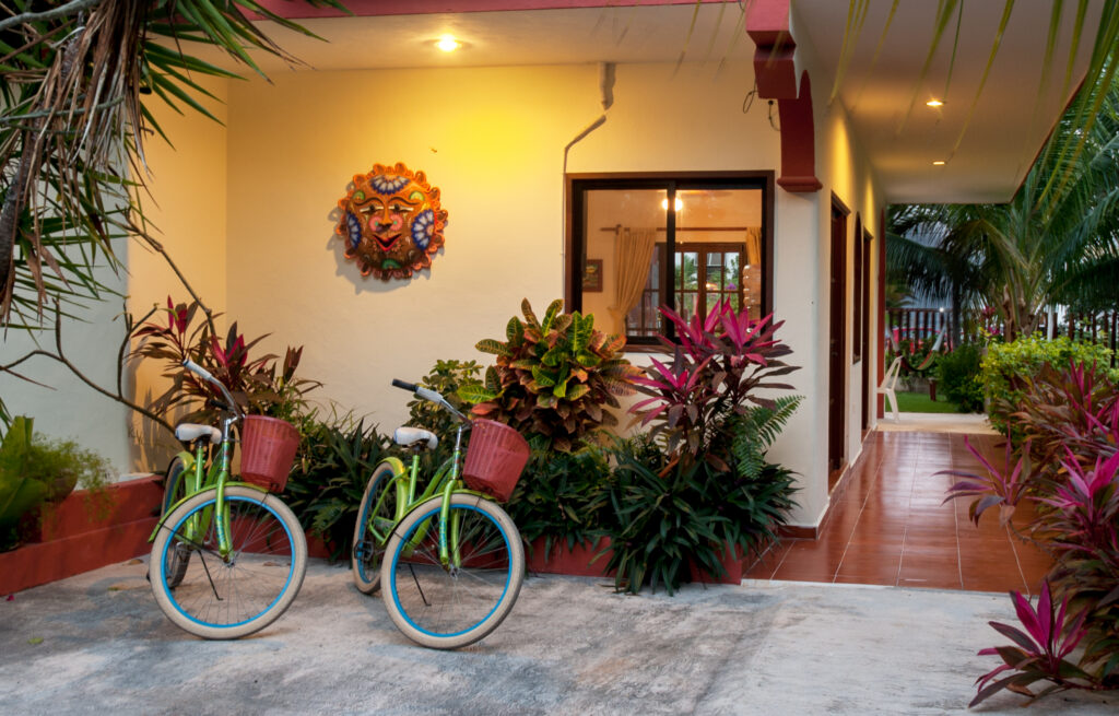 Two bicycles beside tropical plants and a colorful sun wall ornament near the entrance.