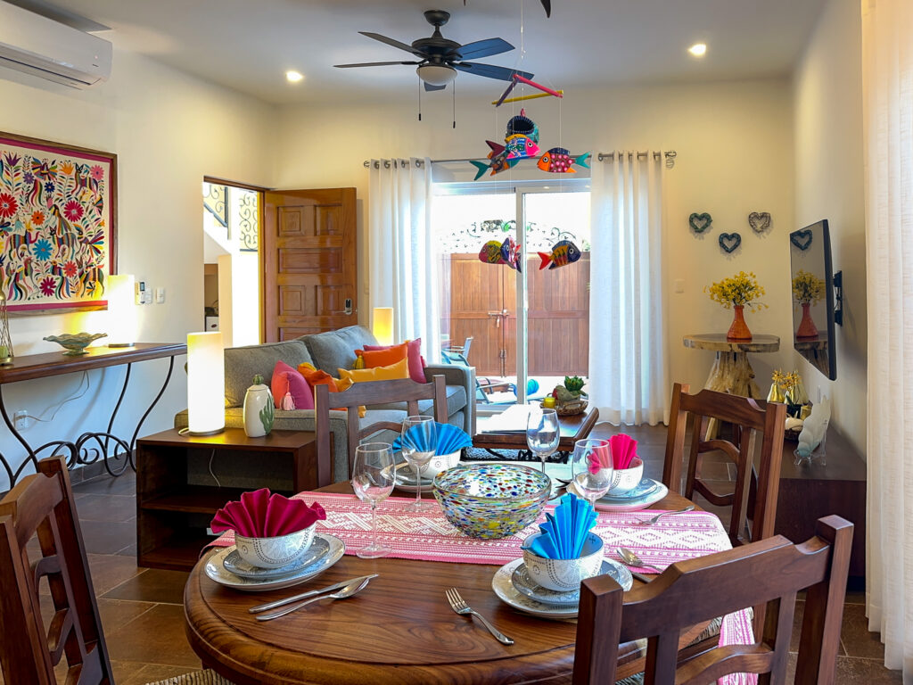 Round wooden dining table set with colorful dishes in front of the sofa and patio doors.