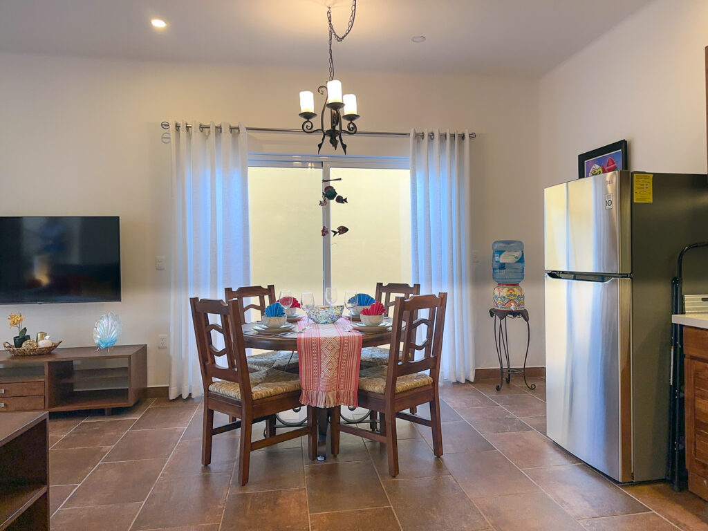 Table set for four beneath a chandelier beside a stainless steel refrigerator and glass doors.