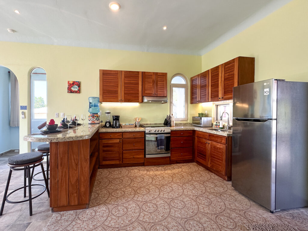 Kitchen with wooden cabinets, stainless steel refrigerator, stove, and curved breakfast counter with stools.
