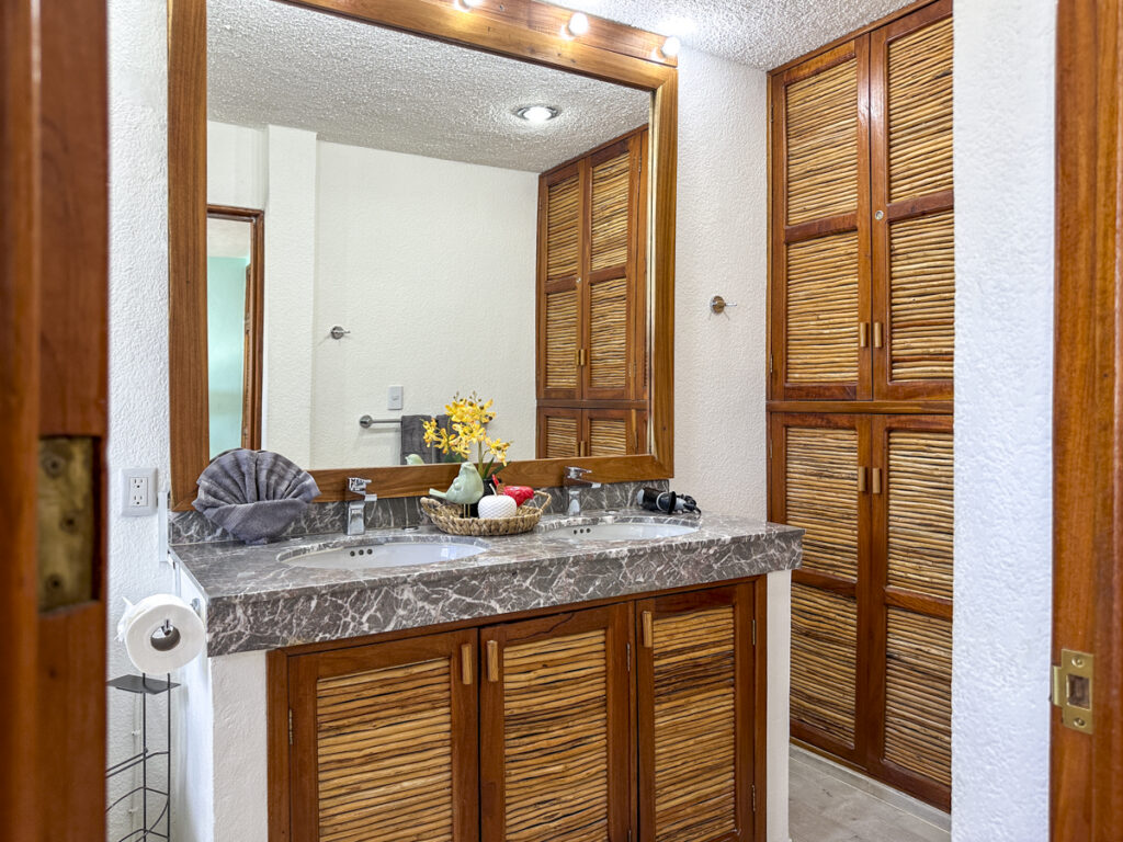 Gray stone bathroom vanity beneath a large mirror beside wooden closet doors.