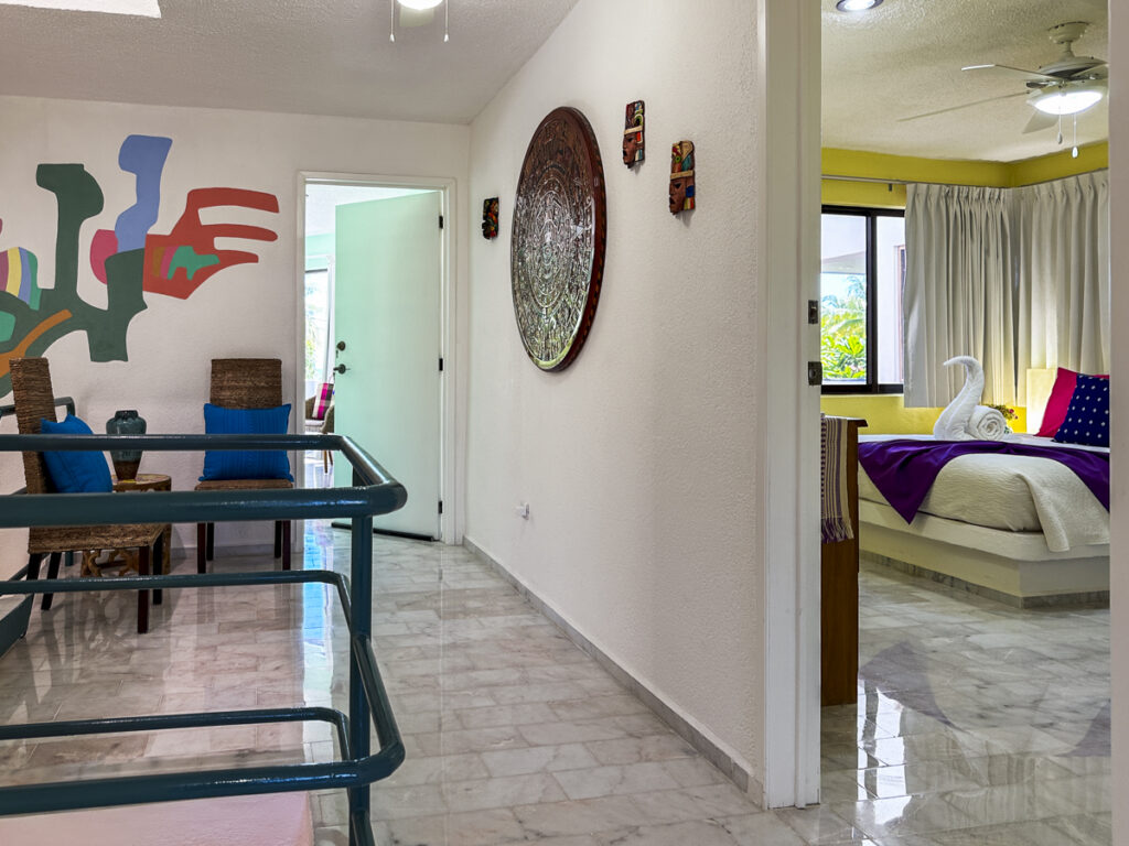 Upstairs landing with teal railings, wall decorations, and a doorway into a bedroom.