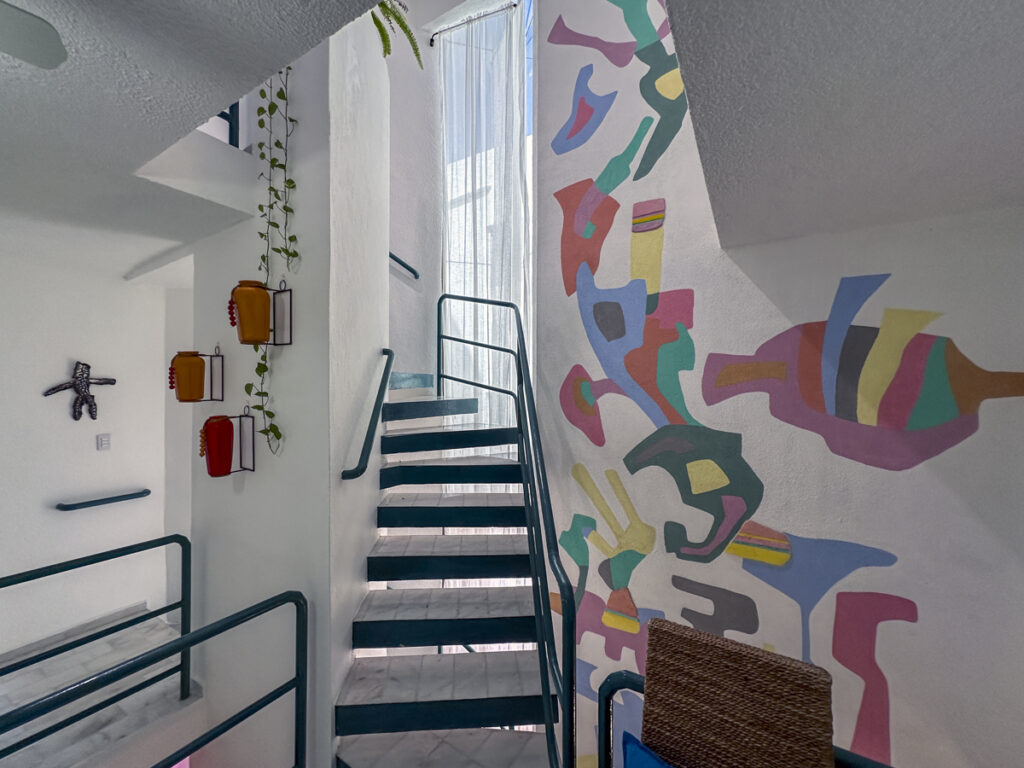 Open staircase with teal railings rising beside a colorful abstract wall mural.