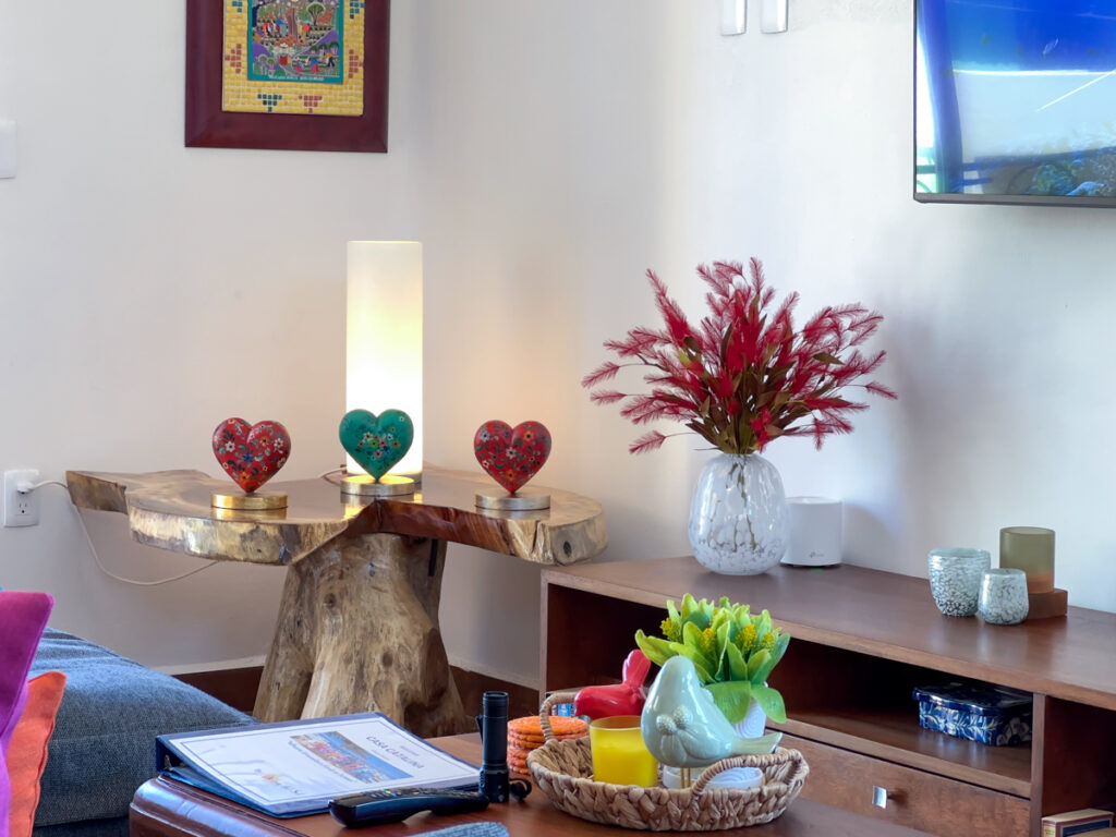 Colorful heart ornaments on a sculptural wooden table beside flowers and a television console.