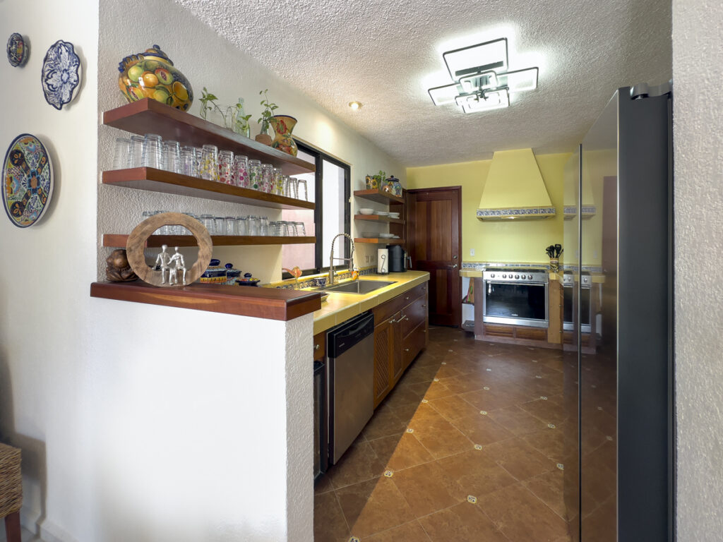 Galley kitchen with yellow counters, wooden cabinets, open glass shelves, and a stove.