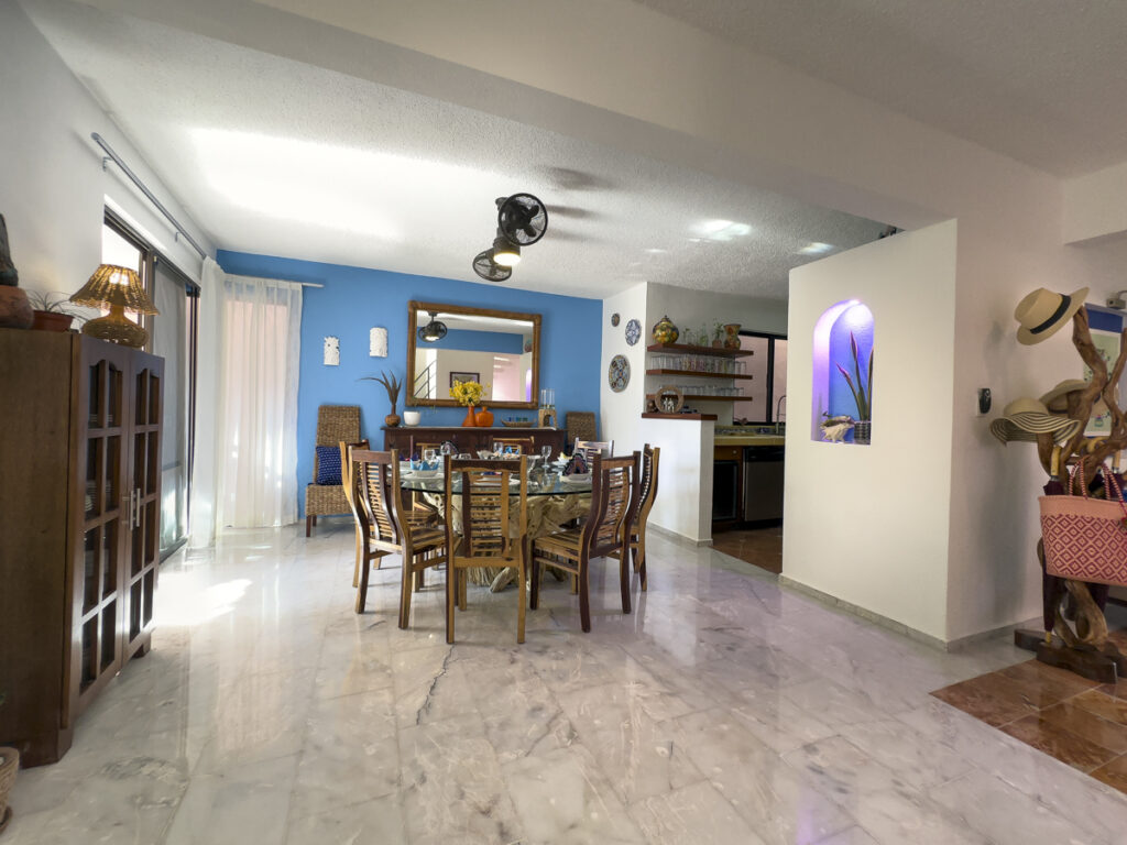 Large dining table with wooden chairs beside a blue accent wall and the entrance hallway.