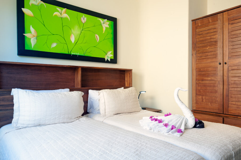 Two beds beneath green floral artwork, with a towel swan and petals on one bed.