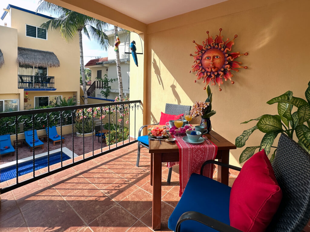 Covered balcony with blue chairs and a small table overlooking the courtyard pool.