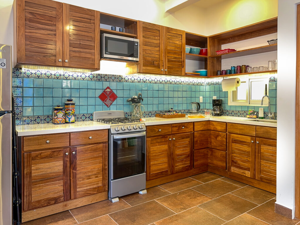 L-shaped kitchen with wooden cabinets, stove, microwave, and a blue patterned tile backsplash.