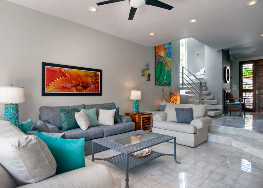 Sofas and a glass-topped coffee table beneath colorful artwork beside the staircase.