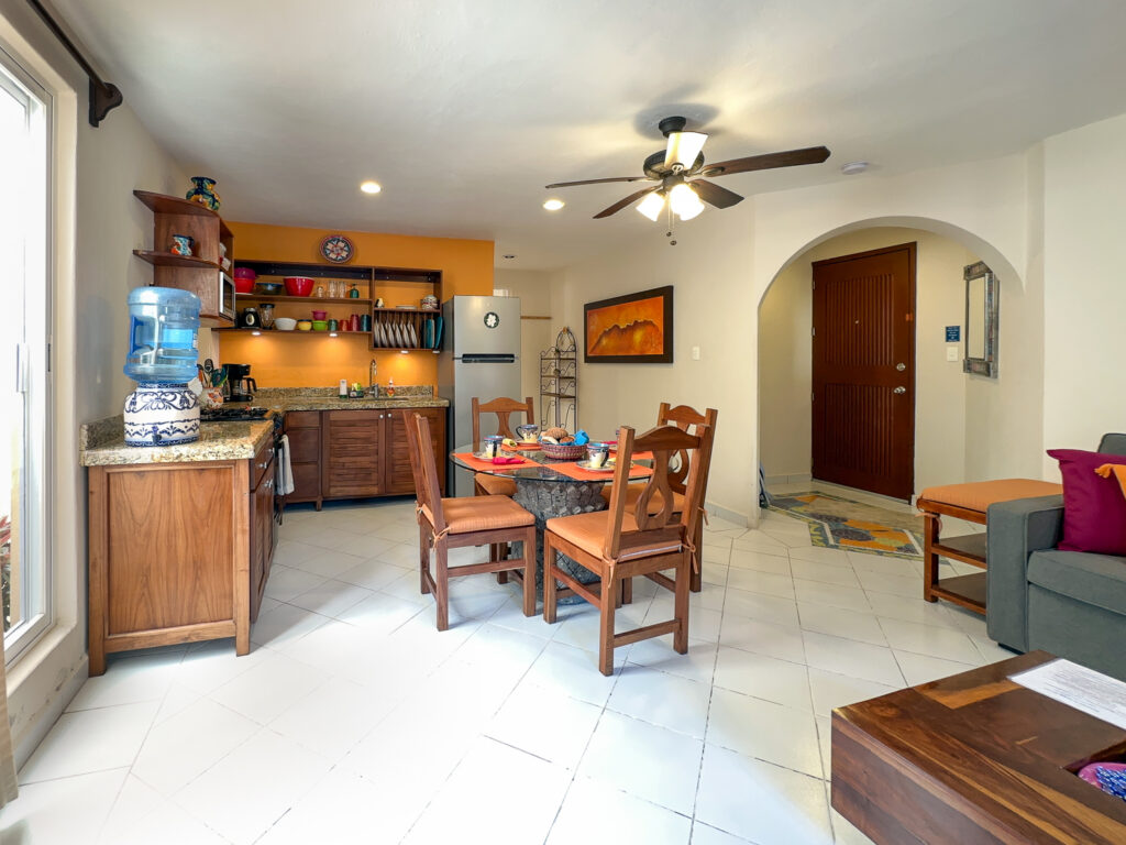 Dining table and kitchen with open shelving near an arched entry area.