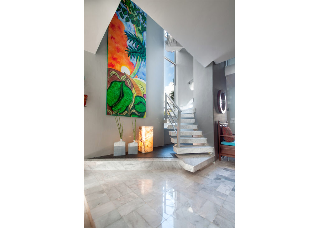 Open staircase with metal railings beside tall colorful artwork in a bright interior.